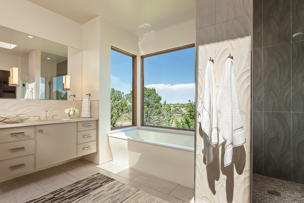 Large contemporary ensuite bathroom in Albuquerque with recessed-panel cabinets, grey cabinets, a freestanding bath, a corner shower, a one-piece toilet, beige tiles, porcelain tiles, white walls, porcelain flooring, a submerged sink and solid surface worktops.
