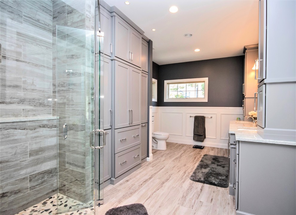 Пример оригинального дизайна: большая главная ванная комната в стиле неоклассика (современная классика) с фасадами с утопленной филенкой, серыми фасадами, душем без бортиков, раздельным унитазом, бежевой плиткой, галечной плиткой, серыми стенами, полом из керамической плитки, врезной раковиной, бежевым полом и душем с распашными дверями