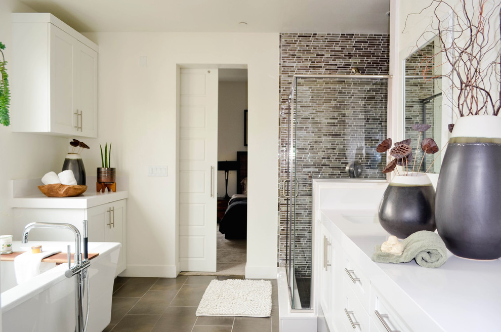 Inspiration for an expansive classic ensuite bathroom in Los Angeles with shaker cabinets, white cabinets, a freestanding bath, an alcove shower, a one-piece toilet, grey tiles, glass sheet walls, white walls, porcelain flooring, a submerged sink, solid surface worktops, grey floors, a hinged door and white worktops.