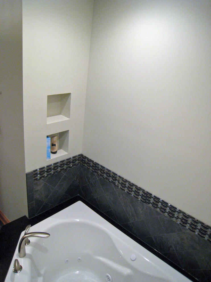 На фото: главная ванная комната среднего размера в стиле модернизм с фасадами с выступающей филенкой, светлыми деревянными фасадами, угловой ванной, душевой комнатой, унитазом-моноблоком, серой плиткой, плиткой из сланца, белыми стенами, полом из сланца, врезной раковиной, столешницей из искусственного кварца, серым полом, душем с распашными дверями и черной столешницей