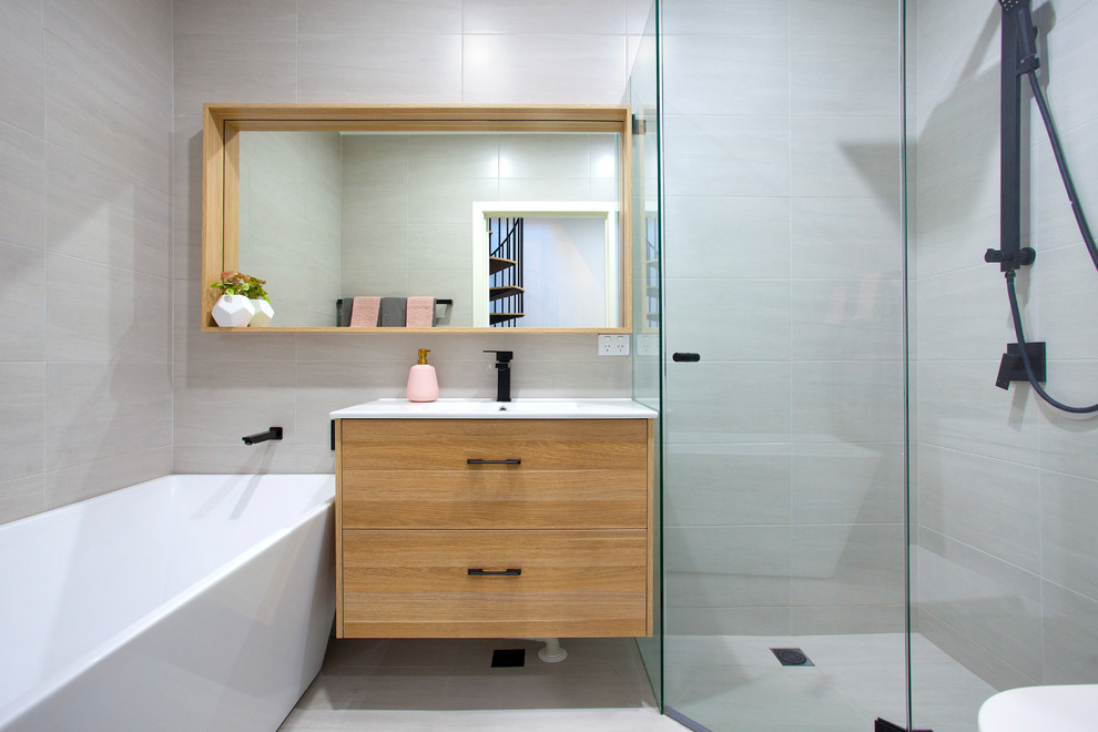 Пример оригинального дизайна: главная ванная комната среднего размера в современном стиле с светлыми деревянными фасадами, угловым душем, серой плиткой, керамогранитной плиткой, плоскими фасадами, отдельно стоящей ванной, душем с распашными дверями, серыми стенами, монолитной раковиной, столешницей из искусственного кварца, белой столешницей и серым полом