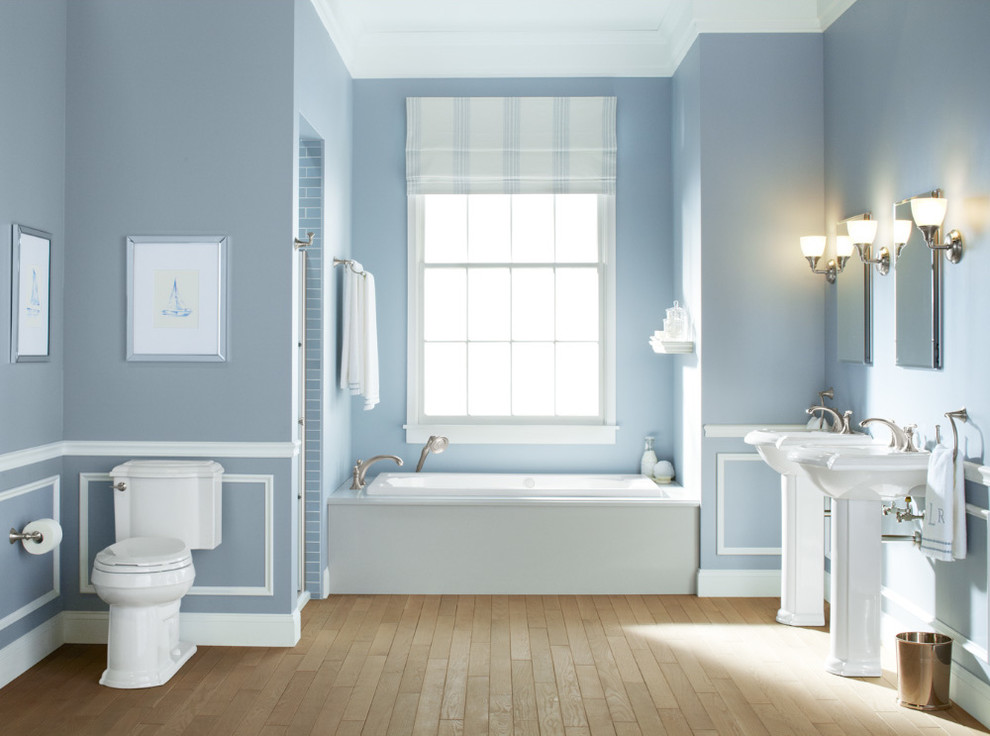 Ejemplo de cuarto de baño principal tradicional de tamaño medio con lavabo con pedestal, bañera empotrada, sanitario de una pieza, paredes azules y suelo de madera clara