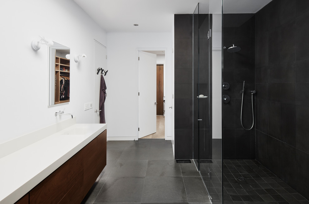 Modernes Duschbad mit flächenbündigen Schrankfronten, dunklen Holzschränken, bodengleicher Dusche, schwarzen Fliesen, weißer Wandfarbe, integriertem Waschbecken, schwarzem Boden, Falttür-Duschabtrennung und weißer Waschtischplatte in Toronto