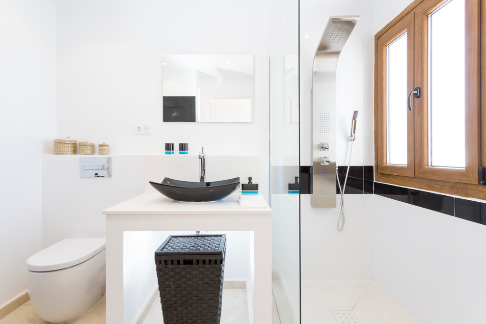 Inredning av ett modernt litet badrum med dusch, med ett fristående handfat, vita väggar, en dusch i en alkov, en toalettstol med hel cisternkåpa, keramikplattor och bänkskiva i akrylsten
