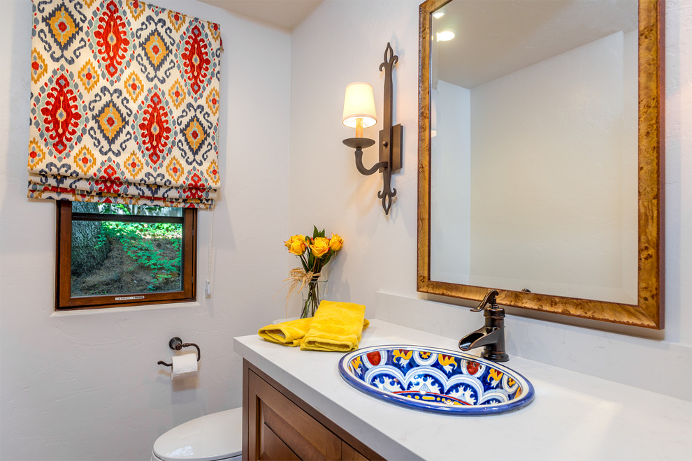 Cette image montre une salle de bain méditerranéenne en bois brun avec un placard avec porte à panneau surélevé, WC suspendus, un carrelage blanc, un mur blanc, un plan de toilette en quartz modifié et un lavabo posé.