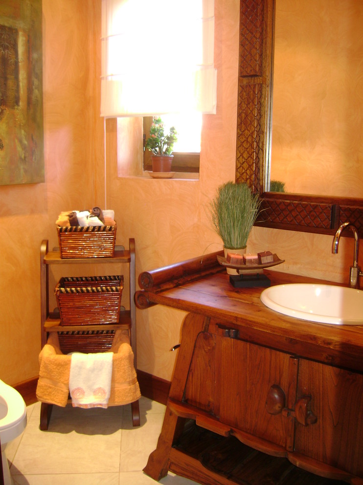 Imagen de cuarto de baño tropical de tamaño medio con armarios tipo mueble, puertas de armario de madera en tonos medios, sanitario de dos piezas, paredes beige, suelo de baldosas de porcelana, lavabo encastrado y encimera de madera