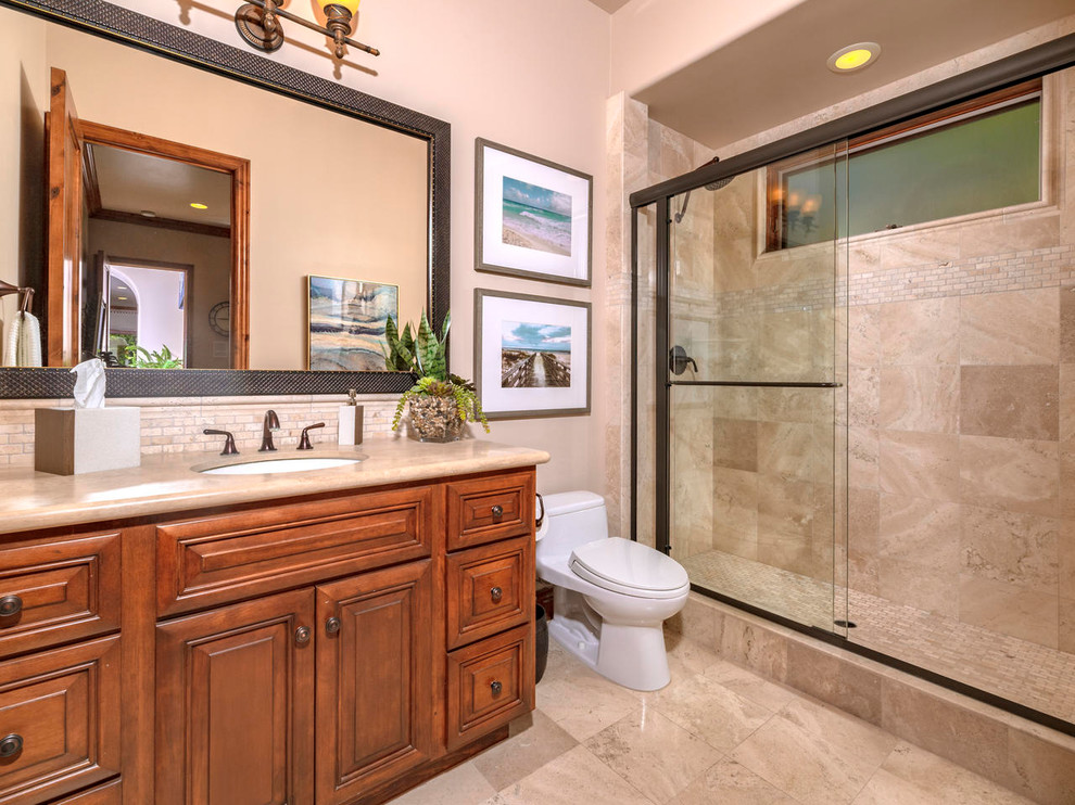На фото: ванная комната среднего размера в средиземноморском стиле с фасадами с выступающей филенкой, коричневыми фасадами, двойным душем, унитазом-моноблоком, бежевой плиткой, плиткой из травертина, бежевыми стенами, полом из травертина, накладной раковиной, столешницей из известняка, бежевым полом, душем с раздвижными дверями и бежевой столешницей с