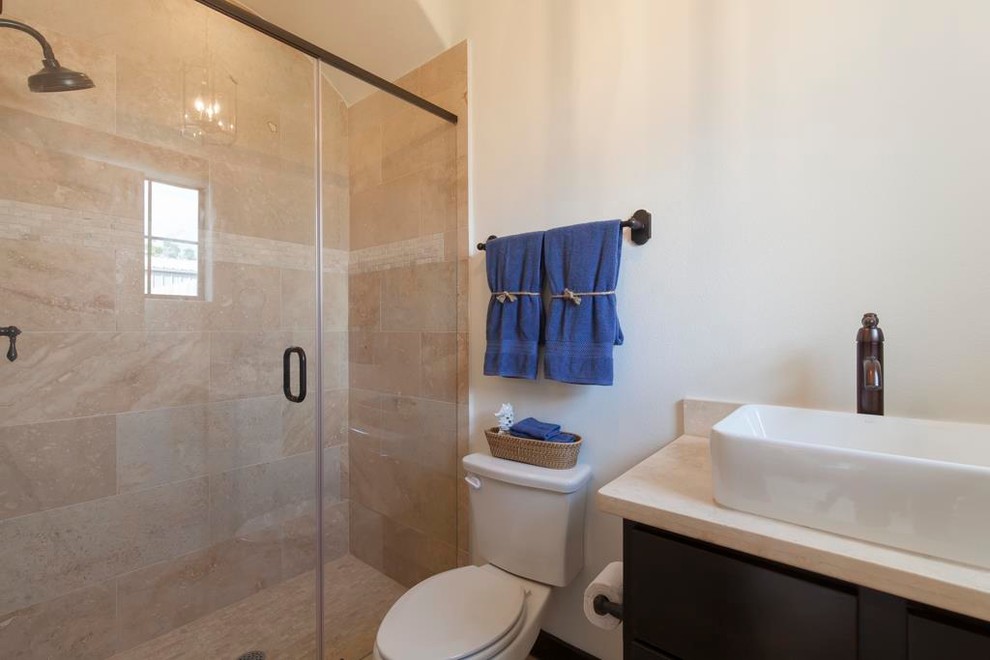 Kleines Mediterranes Badezimmer mit Schrankfronten im Shaker-Stil, dunklen Holzschränken, Toilette mit Aufsatzspülkasten, beigen Fliesen, Steinplatten, weißer Wandfarbe, Travertin, Aufsatzwaschbecken und Quarzit-Waschtisch in Houston