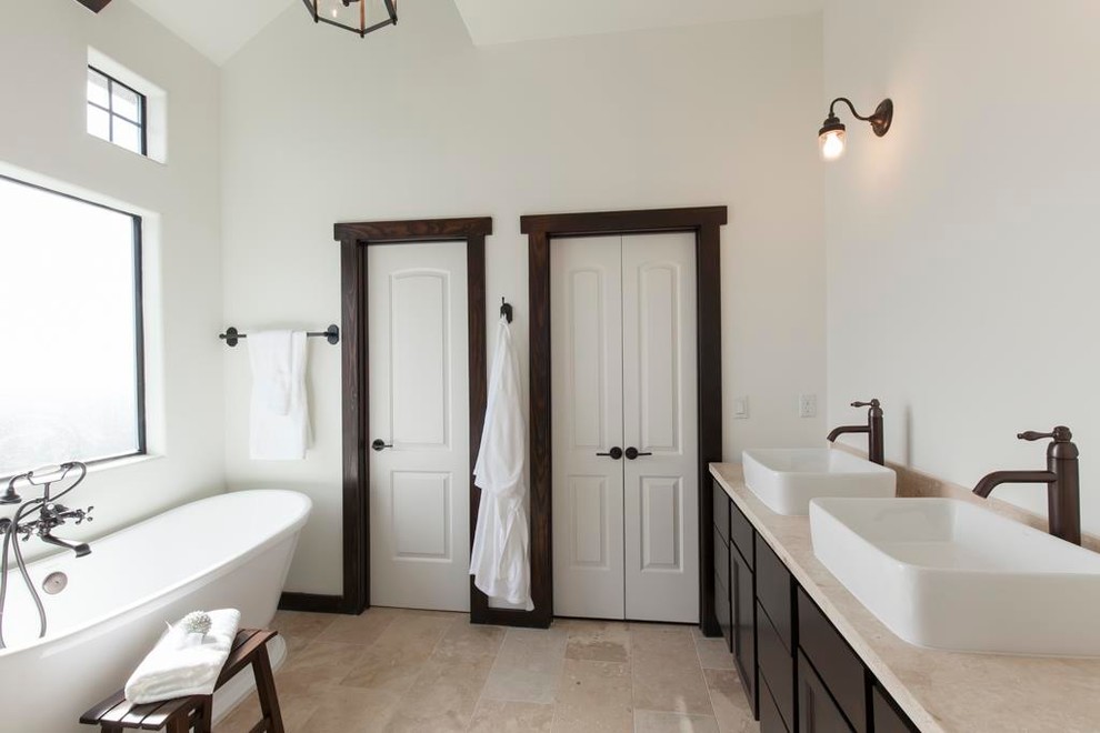 Пример оригинального дизайна: большая главная ванная комната в средиземноморском стиле с темными деревянными фасадами, отдельно стоящей ванной, каменной плиткой, белыми стенами, полом из травертина и настольной раковиной
