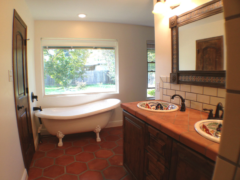 Klassisk inredning av ett en-suite badrum, med ett nedsänkt handfat, luckor med upphöjd panel, skåp i mellenmörkt trä, kaklad bänkskiva, ett badkar med tassar, en öppen dusch, en toalettstol med separat cisternkåpa, perrakottakakel, vita väggar och klinkergolv i terrakotta