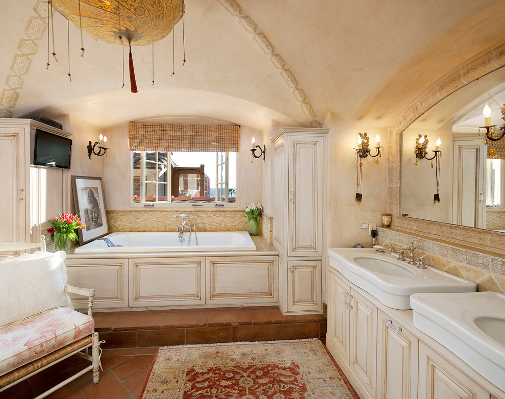 サンタバーバラにある地中海スタイルのおしゃれな浴室 (ベッセル式洗面器、レイズドパネル扉のキャビネット、ベージュのキャビネット、ドロップイン型浴槽) の写真