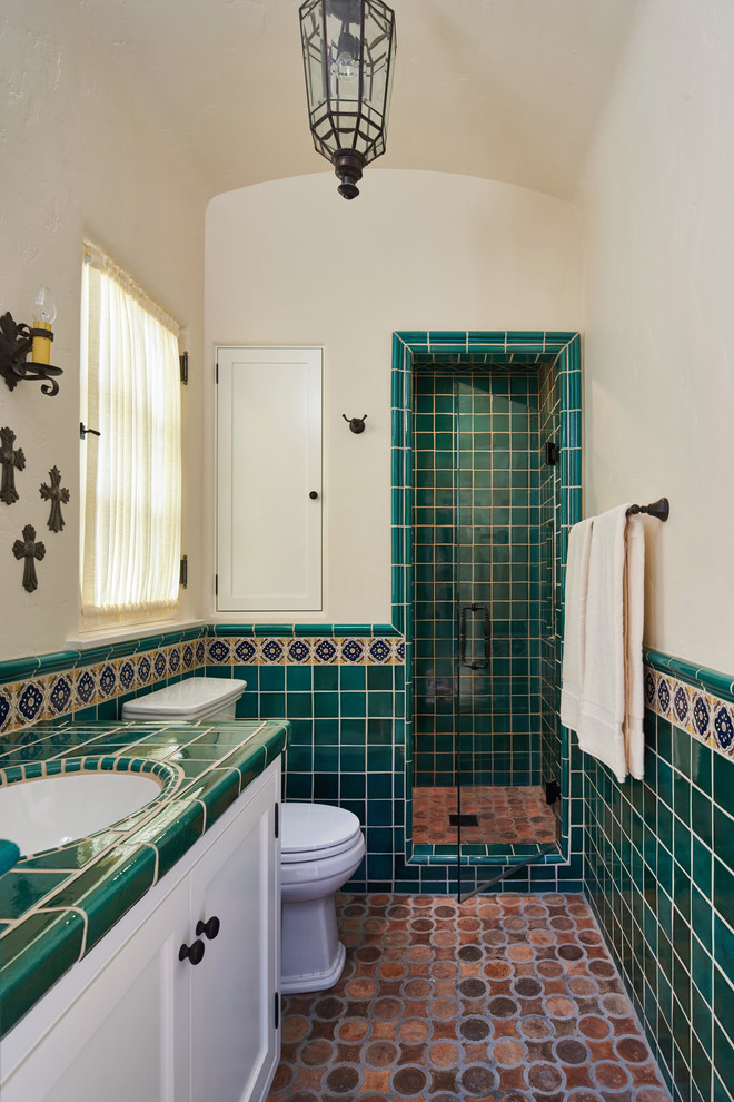 Cette photo montre une salle de bain méditerranéenne de taille moyenne avec un placard à porte shaker, des portes de placard blanches, un carrelage vert, un carrelage multicolore, un mur beige, tomettes au sol, un lavabo encastré, un plan de toilette en carrelage, une cabine de douche à porte battante, un plan de toilette vert et une fenêtre.