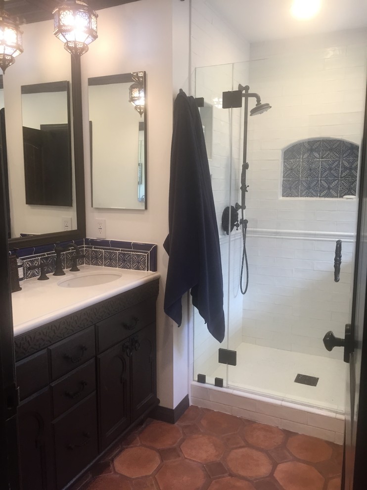 ロサンゼルスにある高級な中くらいなラスティックスタイルのおしゃれなマスターバスルーム (家具調キャビネット、茶色いキャビネット、ドロップイン型浴槽、一体型トイレ	、白いタイル、サブウェイタイル、白い壁、テラコッタタイルの床、オーバーカウンターシンク、クオーツストーンの洗面台、赤い床、開き戸のシャワー) の写真