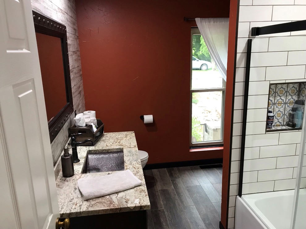 Medium sized mediterranean ensuite bathroom in Cedar Rapids with flat-panel cabinets, dark wood cabinets, an alcove bath, a shower/bath combination, a two-piece toilet, white tiles, metro tiles, orange walls, a submerged sink, engineered stone worktops, a sliding door and beige worktops.