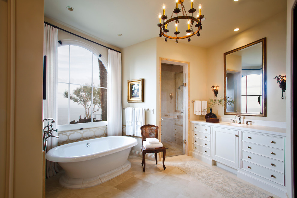 Large mediterranean ensuite bathroom in Los Angeles with recessed-panel cabinets, white cabinets, a freestanding bath, a built-in shower, blue tiles, limestone tiles, white walls, limestone flooring, a submerged sink, marble worktops, beige floors, a hinged door and white worktops.