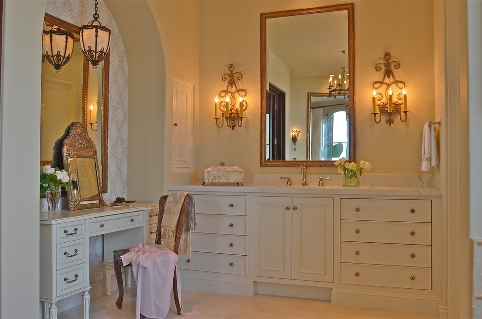 Immagine di una stanza da bagno mediterranea con ante con riquadro incassato, ante bianche, pareti bianche, pavimento in pietra calcarea, lavabo sottopiano, top in marmo, pavimento beige e top bianco