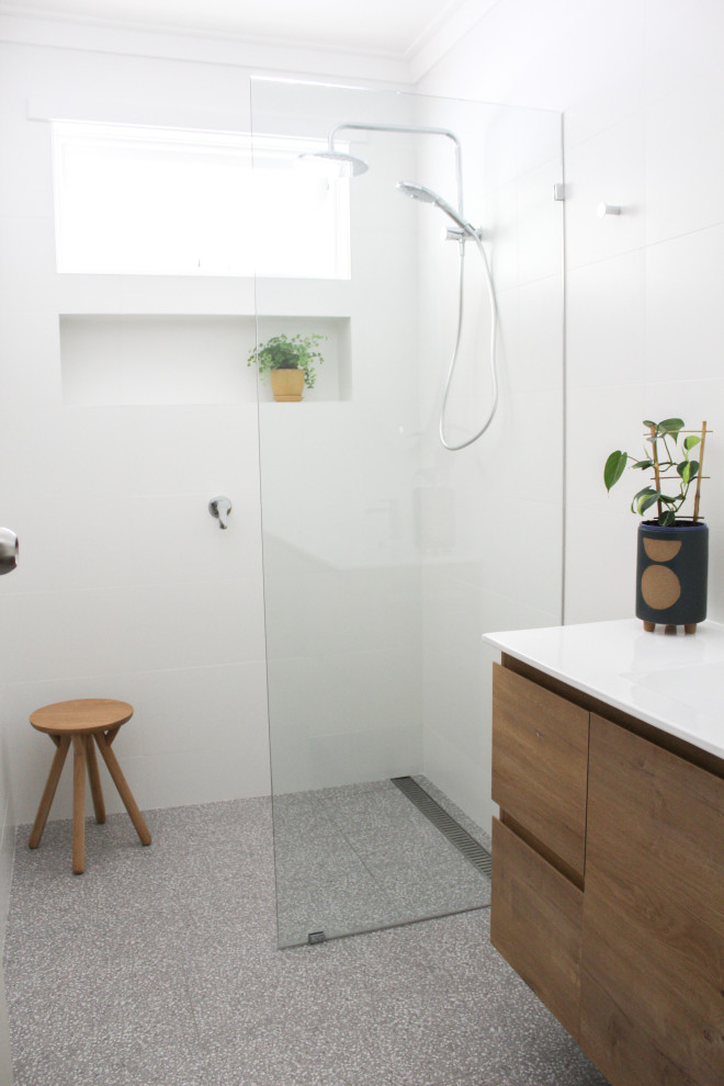 Inredning av ett mellanstort vit vitt badrum för barn, med släta luckor, skåp i mörkt trä, en öppen dusch, vit kakel, keramikplattor, vita väggar, terrazzogolv, ett integrerad handfat, bänkskiva i akrylsten, grått golv och med dusch som är öppen