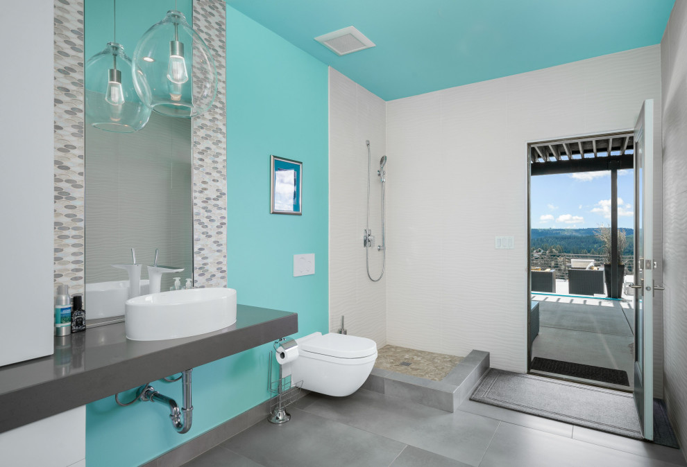 Exempel på ett stort modernt flerfärgad flerfärgat badrum med dusch, med öppna hyllor, grå skåp, ett fristående badkar, en öppen dusch, en vägghängd toalettstol, blå väggar, klinkergolv i porslin, ett fristående handfat, bänkskiva i återvunnet glas, grått golv och med dusch som är öppen