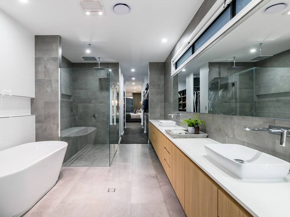 Exemple d'une très grande salle de bain principale tendance en bois clair avec une douche double, un carrelage gris, un mur gris, un sol en carrelage de porcelaine, une vasque, un plan de toilette en quartz modifié, un sol gris, une cabine de douche à porte battante, un plan de toilette blanc, un placard à porte plane et une baignoire indépendante.