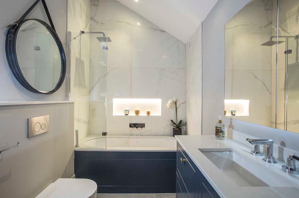 Idées déco pour une salle de bain principale contemporaine de taille moyenne avec un placard à porte shaker, des portes de placard bleues, une baignoire posée, un combiné douche/baignoire, des dalles de pierre, un mur gris, un sol en carrelage de porcelaine, un lavabo suspendu et un plan de toilette en quartz.