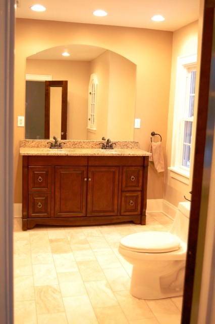 Inspiration for a large traditional ensuite bathroom in Cleveland with freestanding cabinets, medium wood cabinets, a built-in bath, an alcove shower, a two-piece toilet, beige tiles, stone tiles, beige walls, travertine flooring, a submerged sink and granite worktops.
