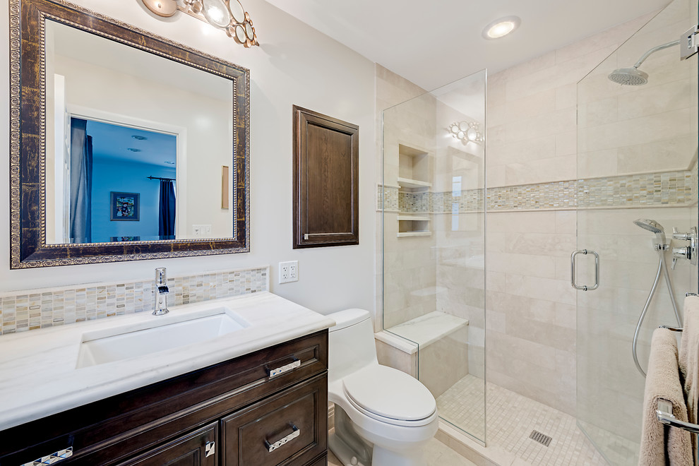 Idées déco pour une salle de bain classique en bois foncé de taille moyenne avec un placard à porte affleurante, WC à poser, un carrelage beige, un carrelage de pierre, un mur blanc, un lavabo encastré et un plan de toilette en marbre.