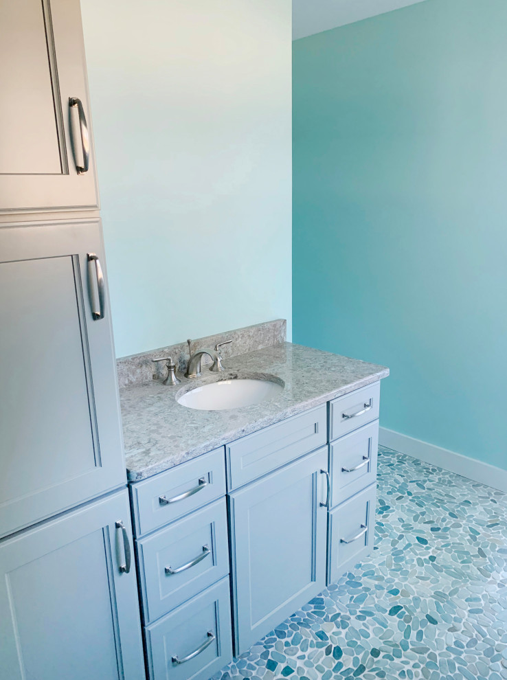 Cette photo montre une salle de bain principale bord de mer de taille moyenne avec un placard à porte shaker, des portes de placard bleues, un mur bleu, un sol en galet, un lavabo intégré, un plan de toilette en marbre, un sol multicolore et un plan de toilette multicolore.