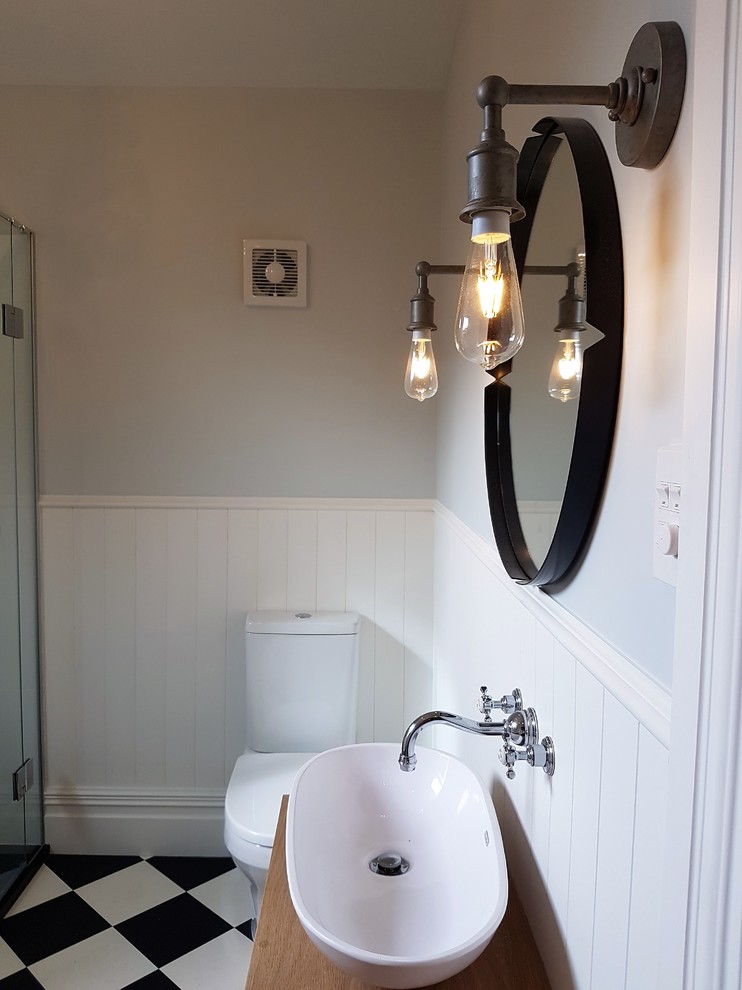 Cette image montre une salle de bain principale victorienne en bois brun de taille moyenne avec un placard en trompe-l'oeil, une baignoire d'angle, une douche d'angle, un carrelage noir et blanc, un mur multicolore, une vasque et un plan de toilette en bois.