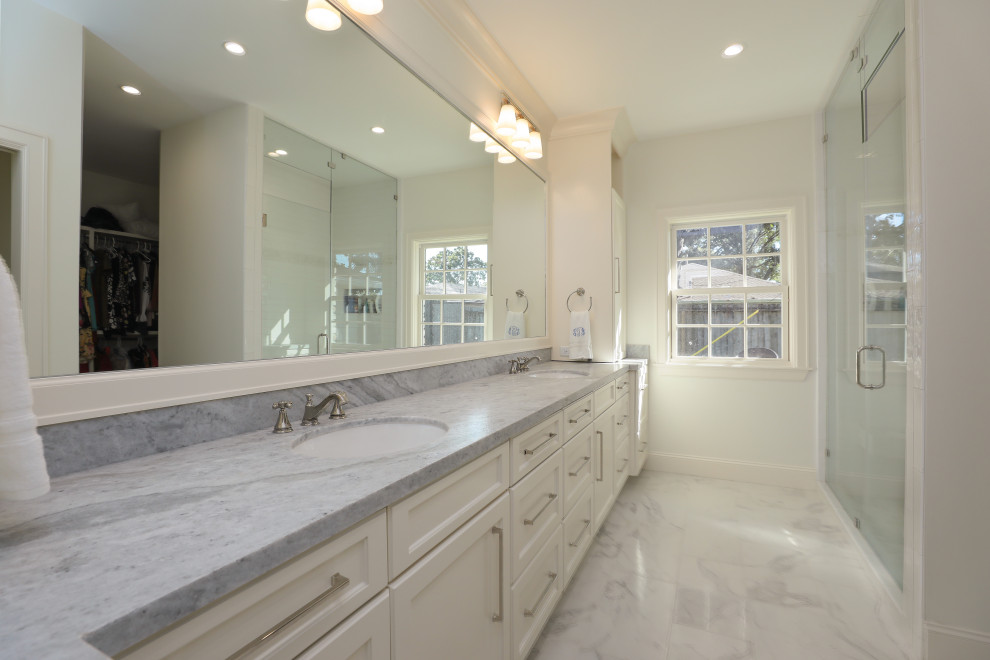 Cette image montre une salle de bain traditionnelle avec un placard à porte plane, des portes de placard blanches, un sol en carrelage de porcelaine, un lavabo encastré, un plan de toilette en marbre et une cabine de douche à porte battante.