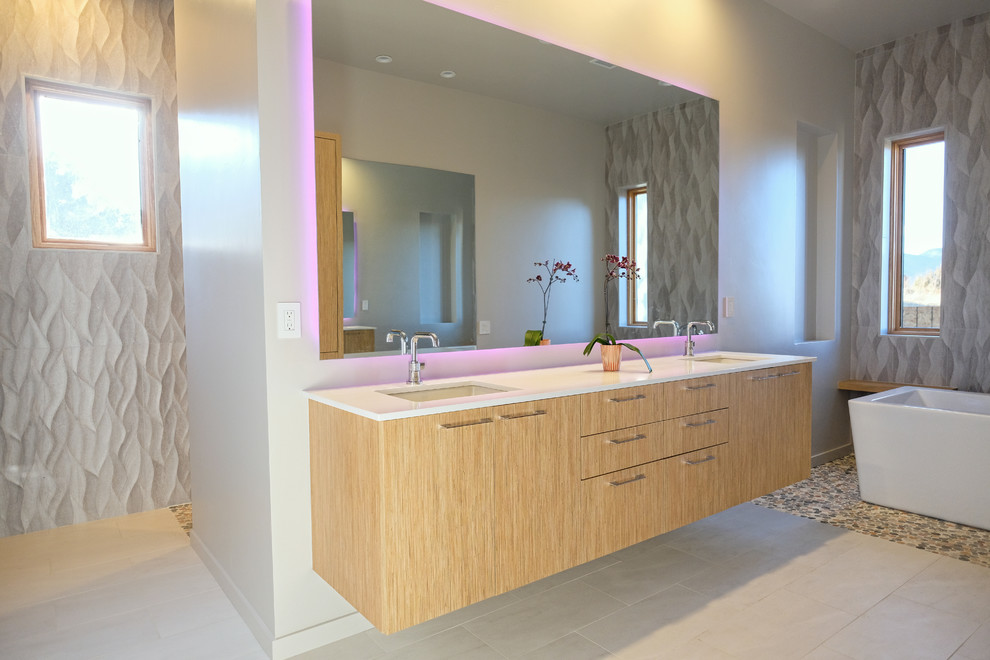 Пример оригинального дизайна: большая главная ванная комната в стиле модернизм с плоскими фасадами, светлыми деревянными фасадами, отдельно стоящей ванной, открытым душем, бежевой плиткой, белыми стенами, полом из керамогранита, врезной раковиной, столешницей из искусственного кварца, бежевым полом, открытым душем и белой столешницей