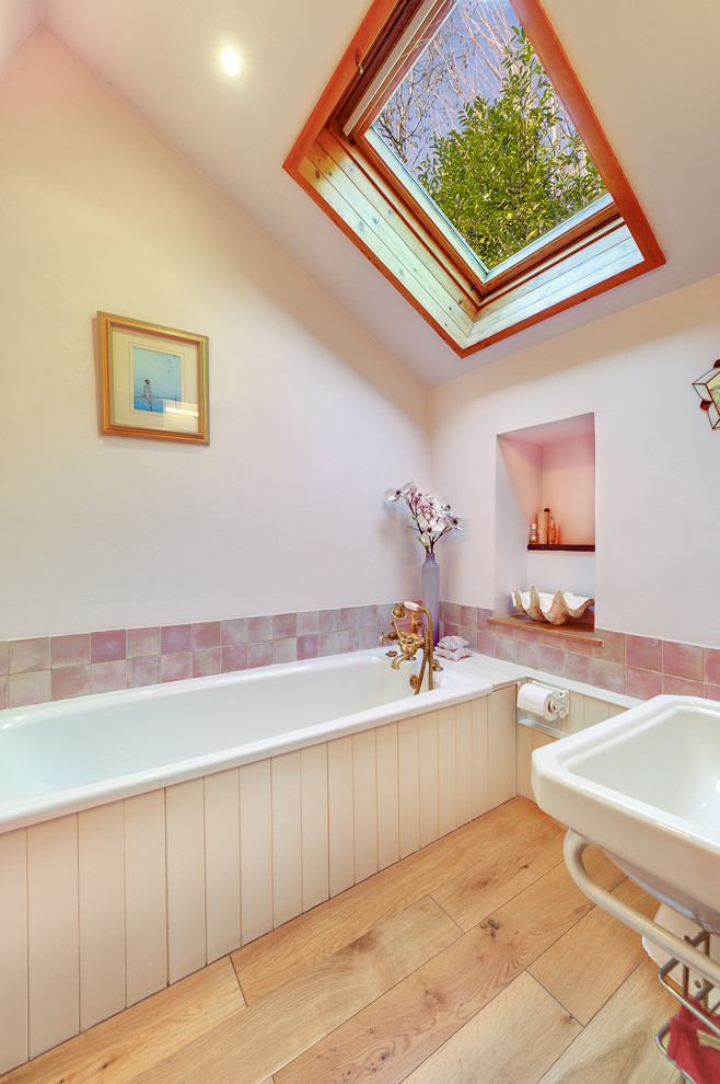 Пример оригинального дизайна: ванная комната в стиле кантри с белыми фасадами, светлым паркетным полом, ванной в нише и розовой плиткой