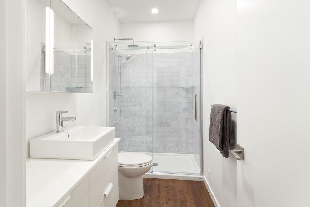 Идея дизайна: ванная комната среднего размера в стиле модернизм с плоскими фасадами, белыми фасадами, душем в нише, унитазом-моноблоком, серой плиткой, мраморной плиткой, белыми стенами, паркетным полом среднего тона, душевой кабиной, настольной раковиной, столешницей из кварцита, коричневым полом и душем с раздвижными дверями