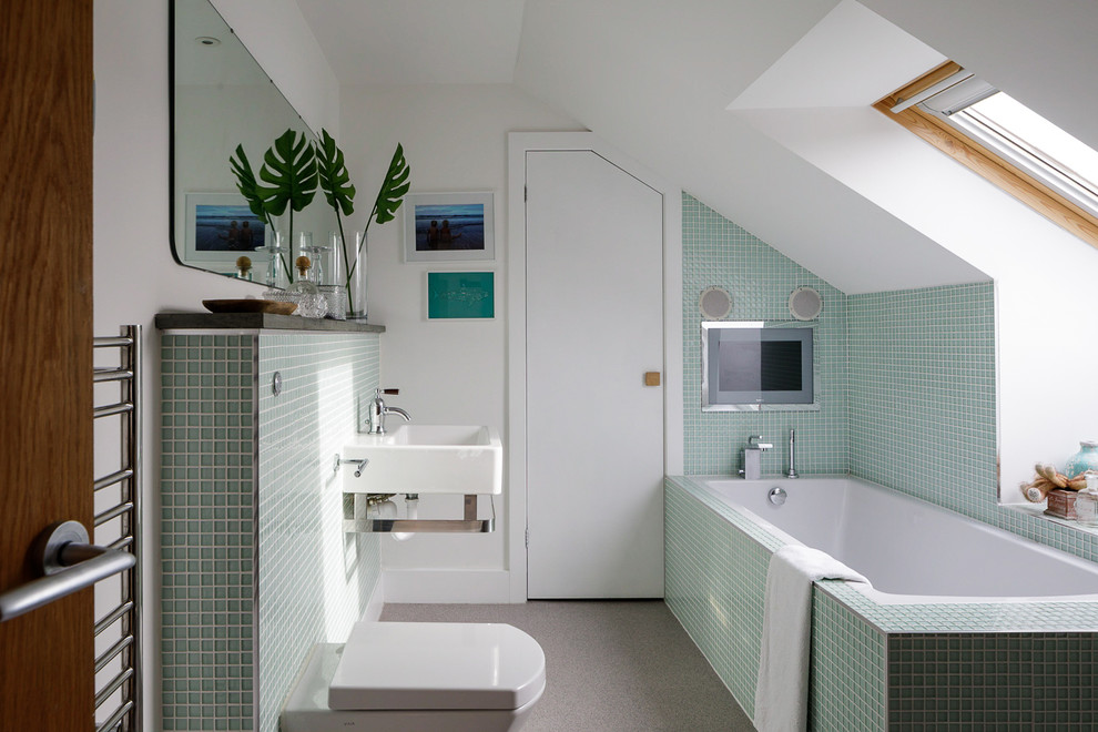 Design ideas for a medium sized contemporary ensuite bathroom in Cornwall with a built-in bath, a wall mounted toilet, green tiles, white walls, a wall-mounted sink and grey floors.