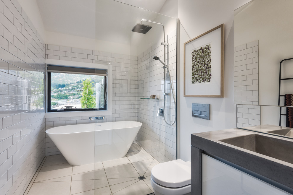 Inspiration for a contemporary ensuite wet room bathroom in Christchurch with flat-panel cabinets, white cabinets, a freestanding bath, a wall mounted toilet, white tiles, metro tiles, white walls, an integrated sink, concrete worktops, beige floors and an open shower.
