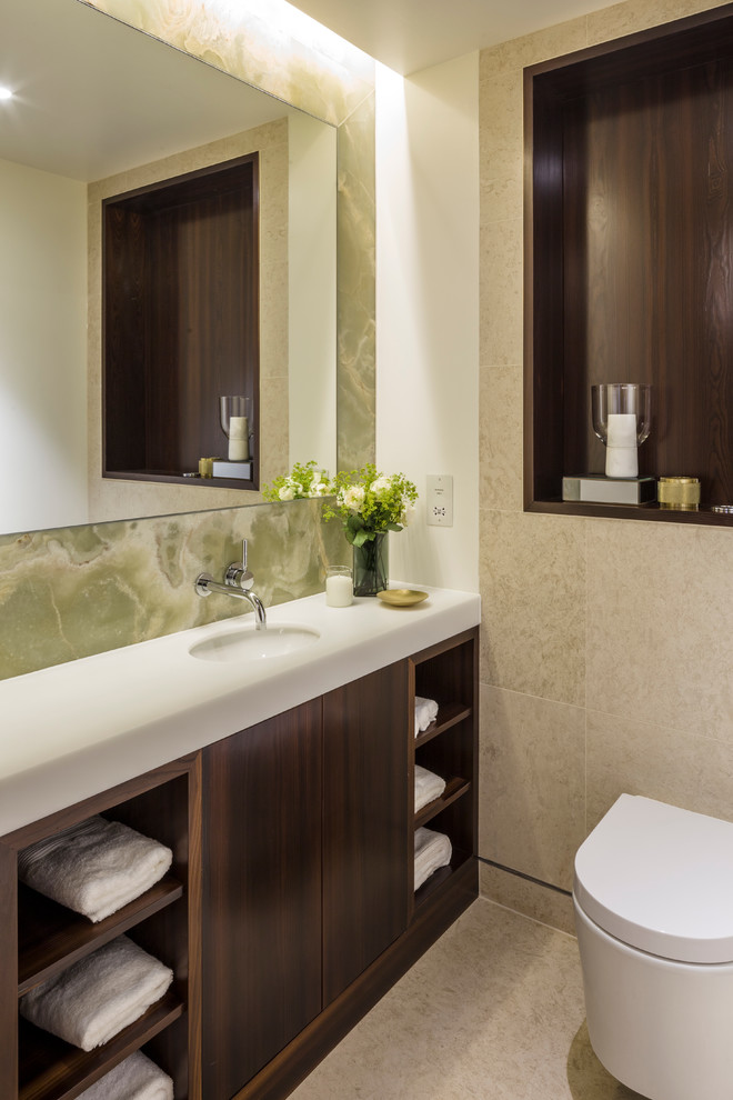 Cette image montre une salle de bain design en bois foncé avec un lavabo encastré, un placard à porte plane, un carrelage beige et un mur blanc.