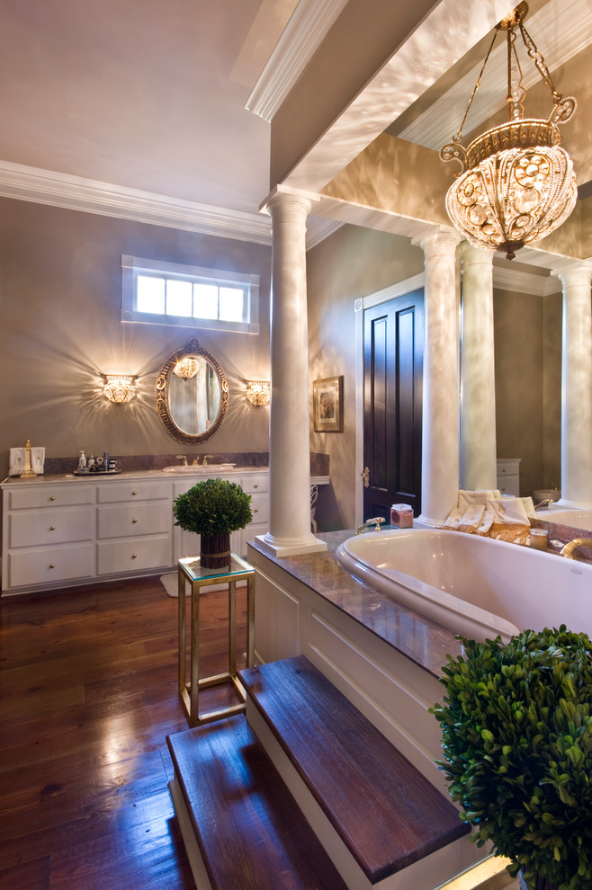 ニューオリンズにある高級な広いトラディショナルスタイルのおしゃれな浴室 (オーバーカウンターシンク、レイズドパネル扉のキャビネット、白いキャビネット、御影石の洗面台、ドロップイン型浴槽、茶色い壁、無垢フローリング) の写真