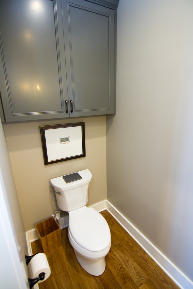 Exemple d'un petit WC et toilettes bord de mer avec un placard avec porte à panneau encastré, des portes de placard grises, WC à poser, un mur gris et un sol en bois brun.