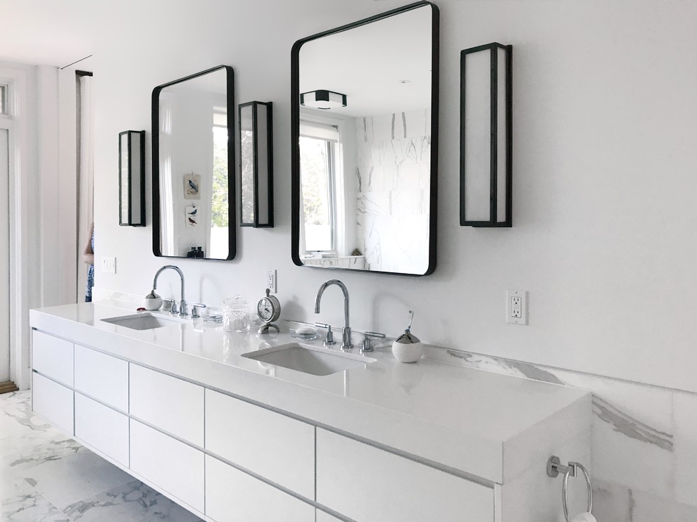 Photo of a large modern ensuite wet room bathroom in Toronto with flat-panel cabinets, white cabinets, a freestanding bath, a wall mounted toilet, white tiles, marble tiles, white walls, marble flooring, a submerged sink, solid surface worktops, white floors and a hinged door.