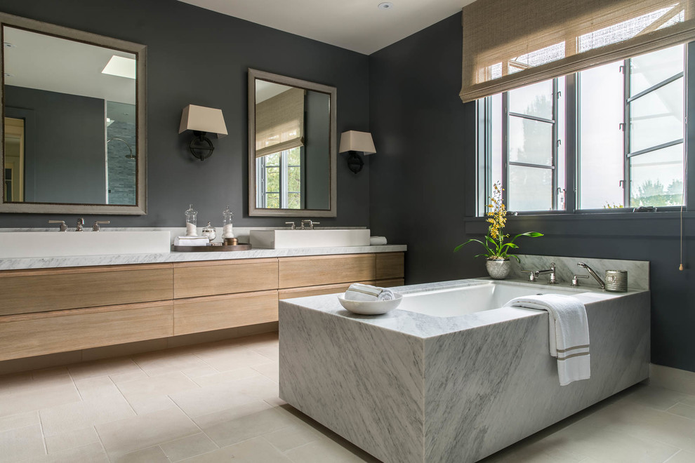 Cette image montre une salle de bain principale design en bois brun avec une baignoire indépendante, un sol en carrelage de céramique, une vasque, un plan de toilette en marbre, un placard à porte plane et un mur gris.