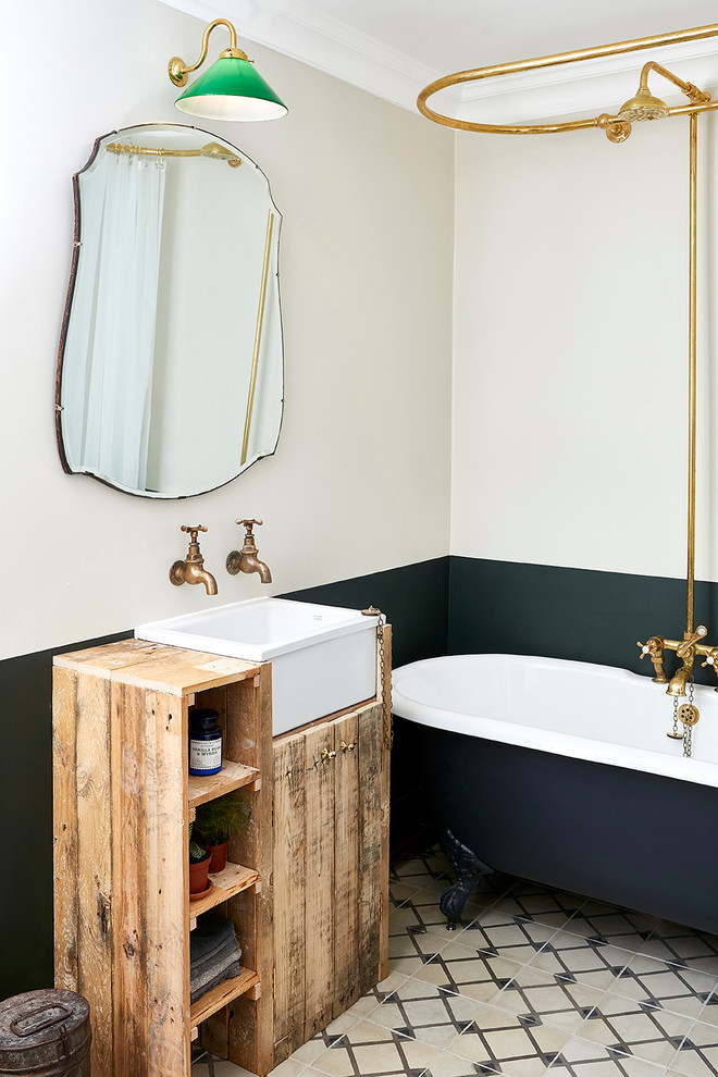 Bild på ett litet vintage brun brunt badrum för barn, med skåp i slitet trä, ett badkar med tassar, en dusch/badkar-kombination, flerfärgade väggar, cementgolv, ett avlångt handfat, flerfärgat golv, dusch med duschdraperi, träbänkskiva och släta luckor