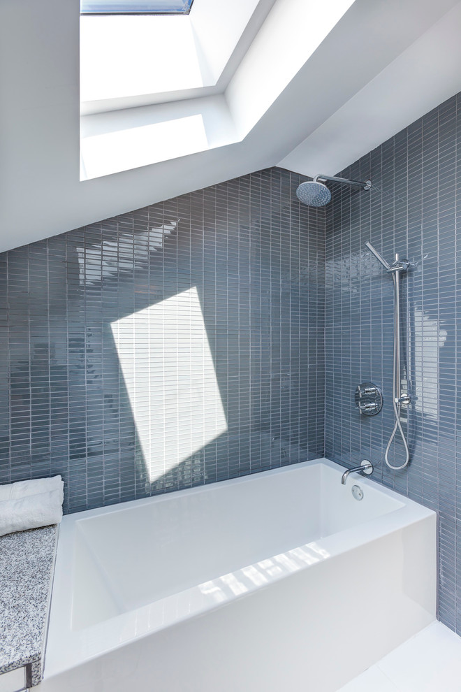 Cette photo montre une salle de bain tendance avec un placard à porte plane, des portes de placard blanches, un plan de toilette en granite, une baignoire en alcôve, un combiné douche/baignoire, un carrelage gris, mosaïque, un mur gris et un sol en carrelage de céramique.