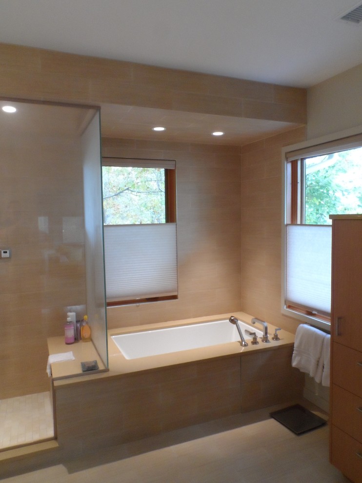 This is an example of a medium sized contemporary ensuite bathroom in Baltimore with flat-panel cabinets, light wood cabinets, a built-in bath, a shower/bath combination, beige tiles, stone tiles, beige walls and ceramic flooring.