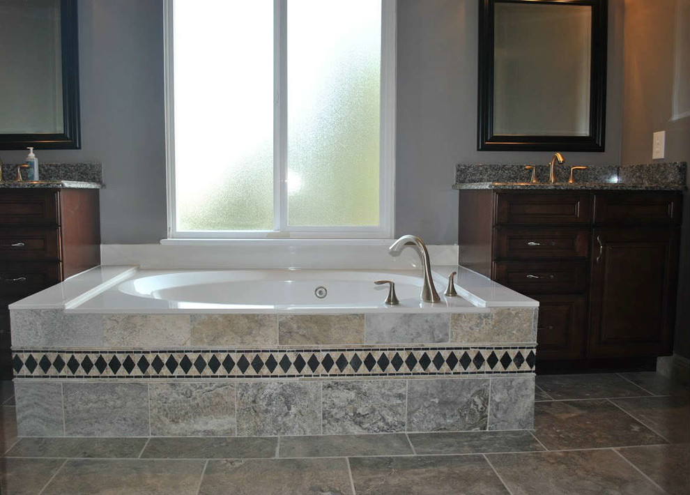 Example of a mid-sized transitional master brown tile, gray tile and slate tile slate floor drop-in bathtub design in St Louis with raised-panel cabinets, dark wood cabinets, gray walls, an undermount sink and granite countertops