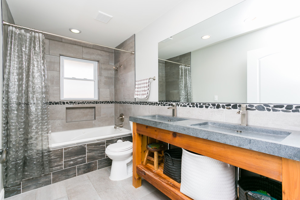 Bild på ett stort funkis badrum, med skåp i mellenmörkt trä, en dusch/badkar-kombination, grå kakel, keramikplattor, grå väggar, klinkergolv i keramik, granitbänkskiva, öppna hyllor, ett badkar i en alkov, en toalettstol med separat cisternkåpa och ett integrerad handfat