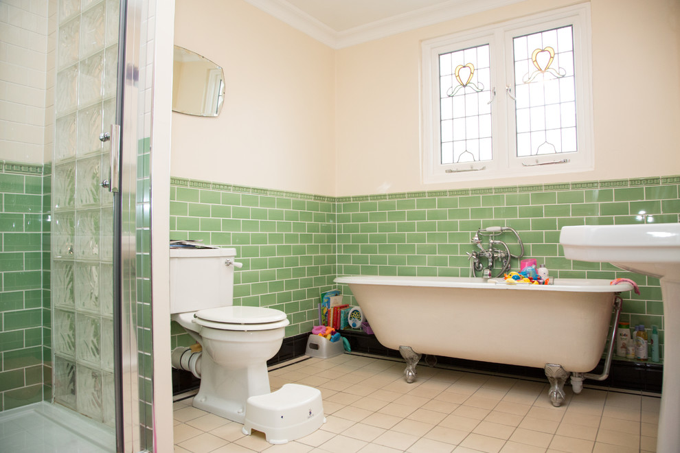 На фото: детская ванная комната среднего размера в викторианском стиле с ванной на ножках, угловым душем, унитазом-моноблоком, зеленой плиткой, керамической плиткой, бежевыми стенами, полом из керамической плитки, раковиной с пьедесталом, бежевым полом и душем с раздвижными дверями с
