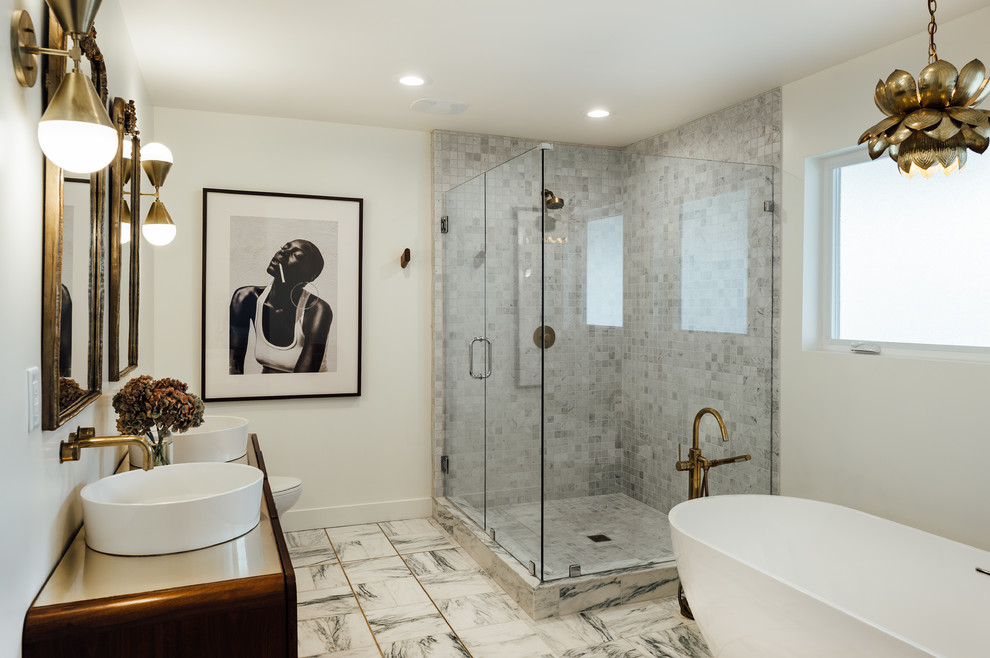 Cette image montre une grande salle de bain principale bohème en bois foncé avec une baignoire indépendante, une douche d'angle, un carrelage gris, du carrelage en marbre, un mur blanc, un sol en marbre, une vasque, une cabine de douche à porte battante et un sol blanc.