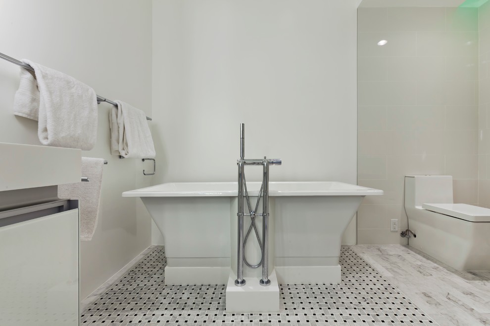 Photo of a medium sized contemporary ensuite bathroom in Minneapolis with a submerged sink, glass-front cabinets, white cabinets, solid surface worktops, a freestanding bath, an alcove shower, a one-piece toilet, multi-coloured tiles, stone tiles, white walls and marble flooring.