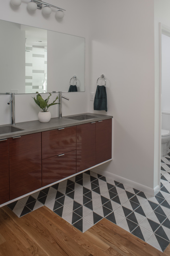 Mid-sized trendy master medium tone wood floor and multicolored floor bathroom photo in Other with flat-panel cabinets, dark wood cabinets, a two-piece toilet, white walls, an integrated sink and soapstone countertops
