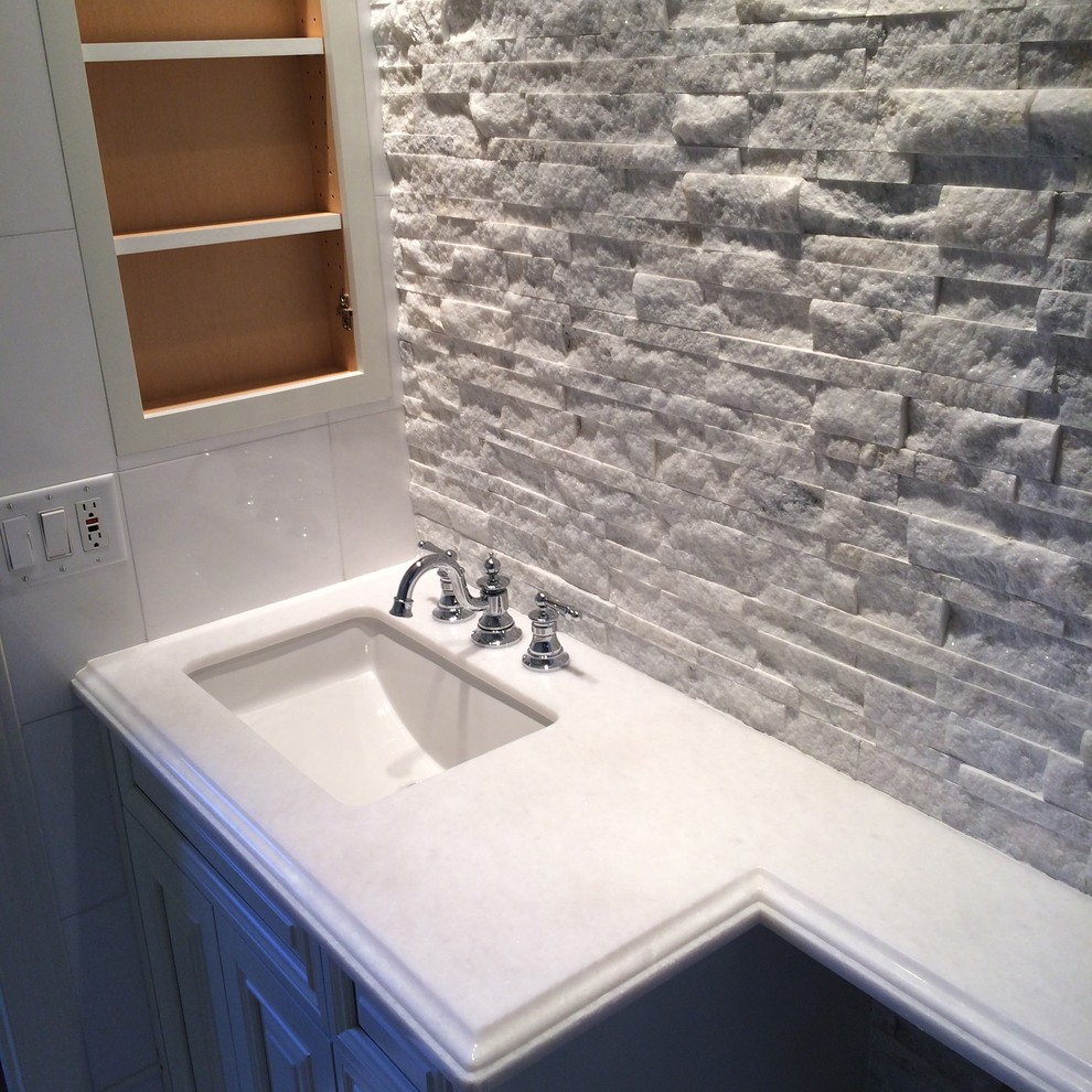 Exemple d'une salle d'eau chic avec un placard avec porte à panneau surélevé, des portes de placard blanches, un lavabo encastré et un plan de toilette en marbre.