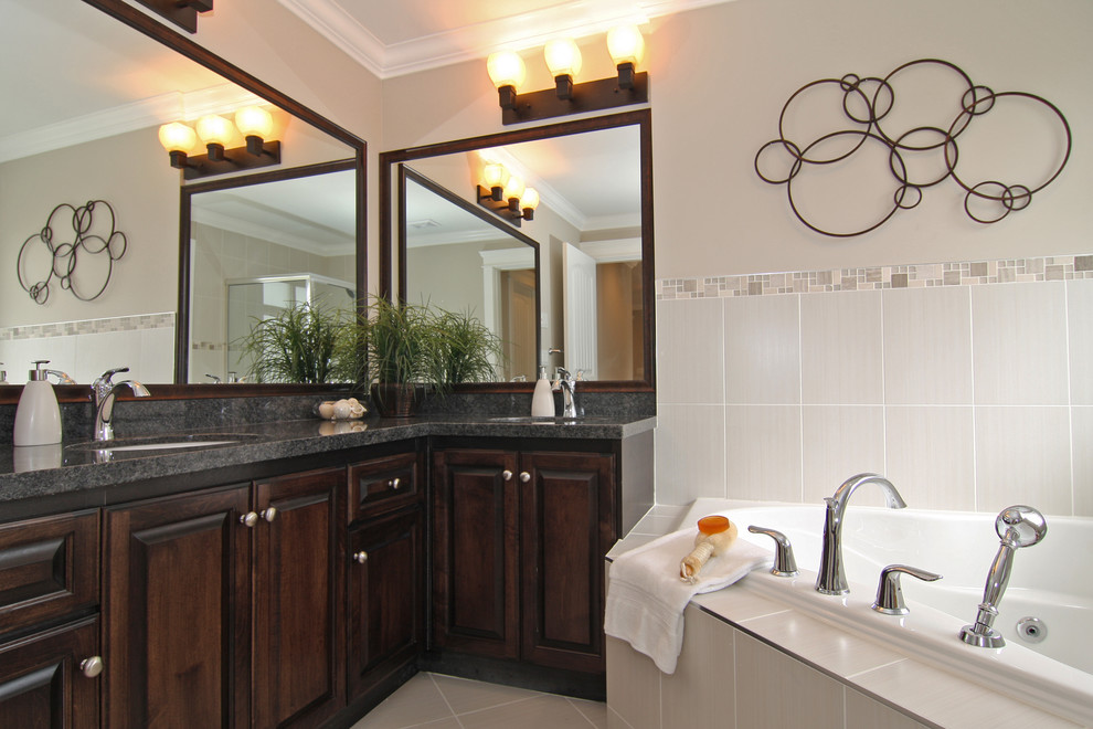 Inspiration pour une salle de bain traditionnelle en bois foncé avec un lavabo encastré, un placard avec porte à panneau surélevé, une baignoire posée et un carrelage gris.